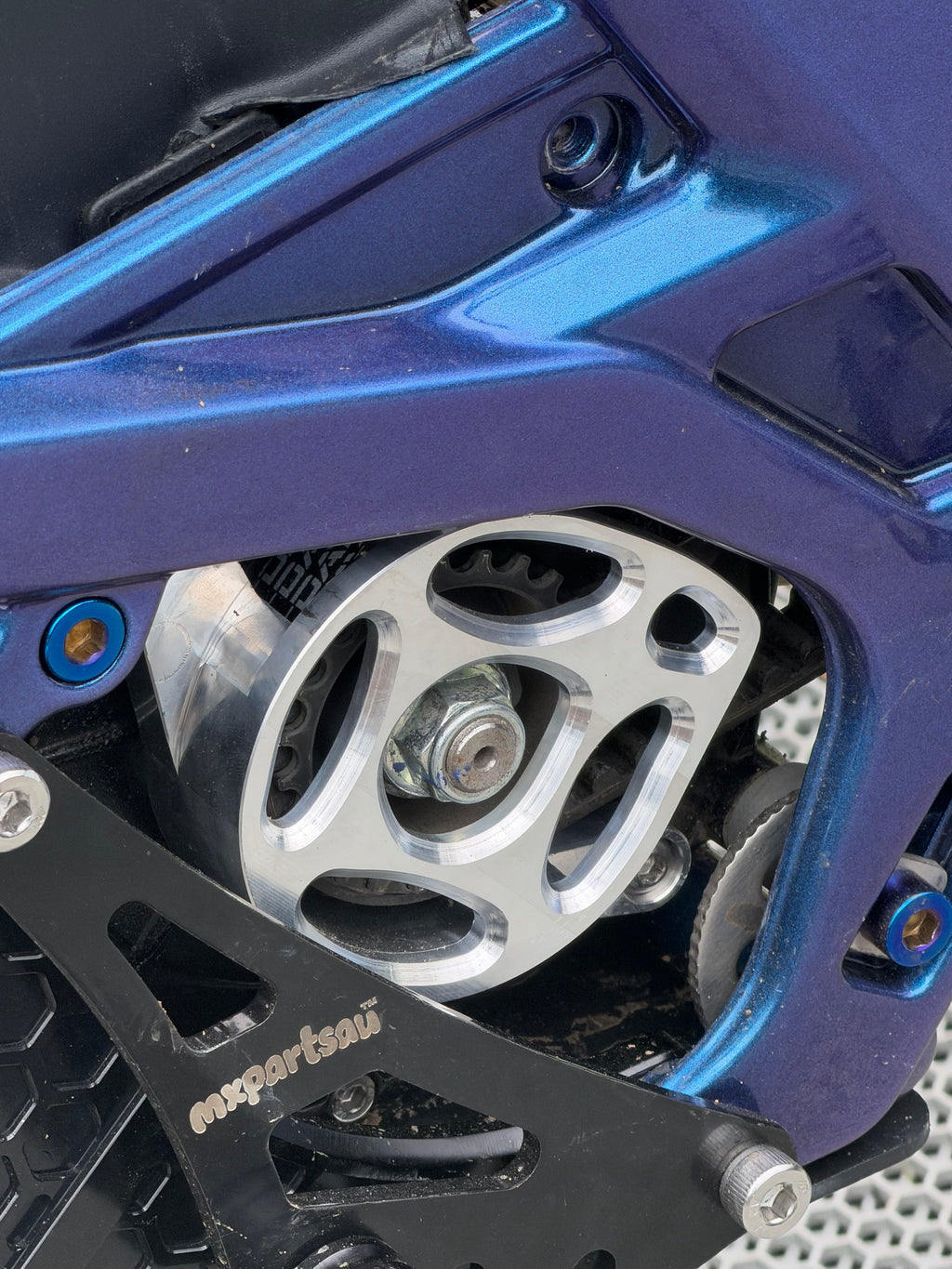 Machined metal motor cover fitted to a blue Surron LBX, shown installed on the bike