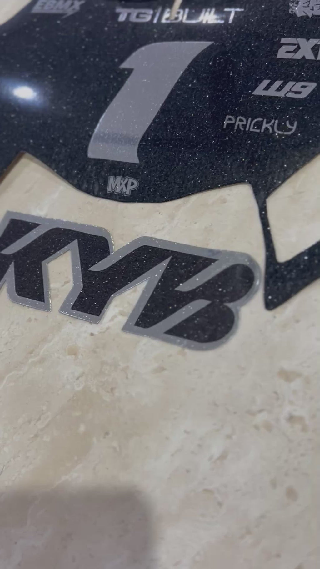 KYB fork sticker in black and silver vinyl shown beside a black glitter plate decal