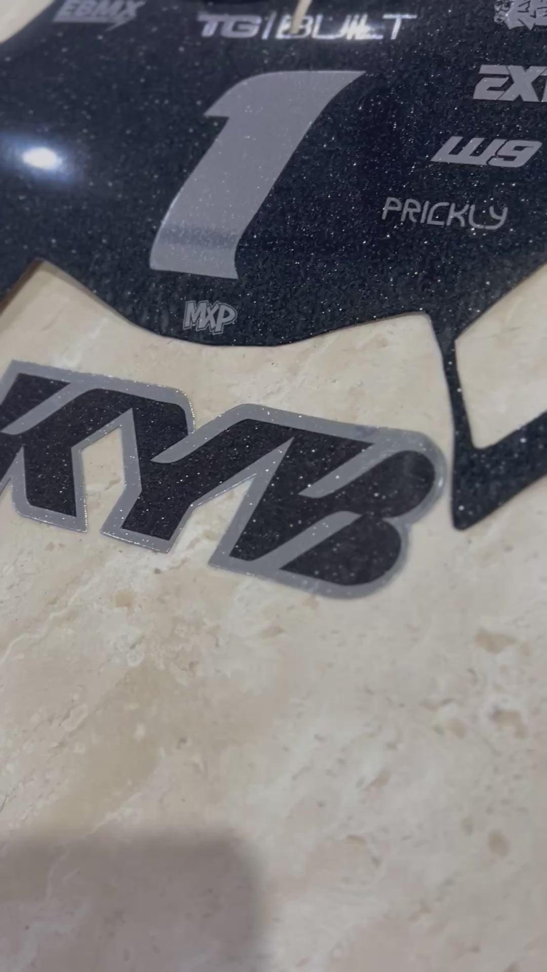 KYB fork sticker in black and silver vinyl shown beside a black glitter plate decal